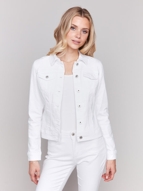 Woman wearing a white denim jacket over a white top and white pants, posing against a light gray background.