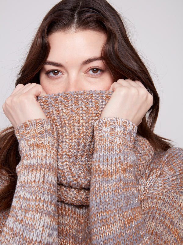 Model wearing fog-colored sweater playfully hiding behind its cozy, textured knit fabric scarf by Charlie B.