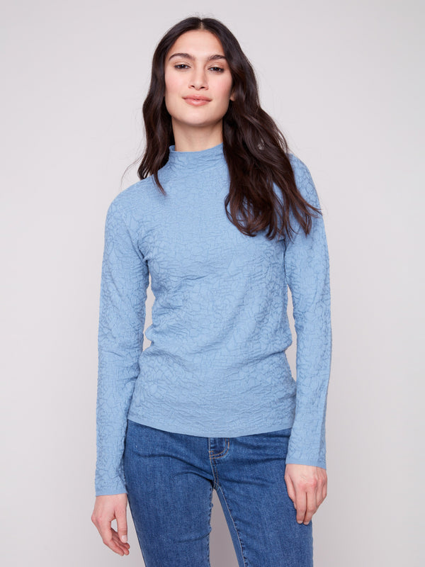 Oxford blue sweater featuring a mock neck paired with classic blue jeans, showcasing its elegant design by Charlie B.
