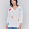 White V-neck knit top with colorful floral appliqués, featuring drop shoulders, by Charlie B.